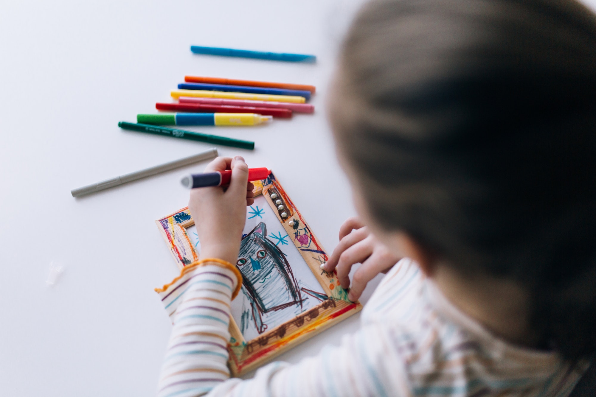 A girl sits at a table and draws, decorates a frame for a photo with drawing, children creativity